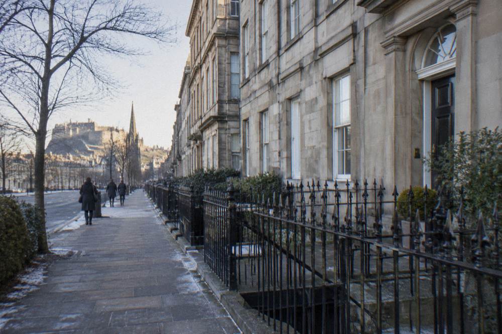 Snowy pavement along Georgian terrace houses with a castle in the distance and few pedestrians