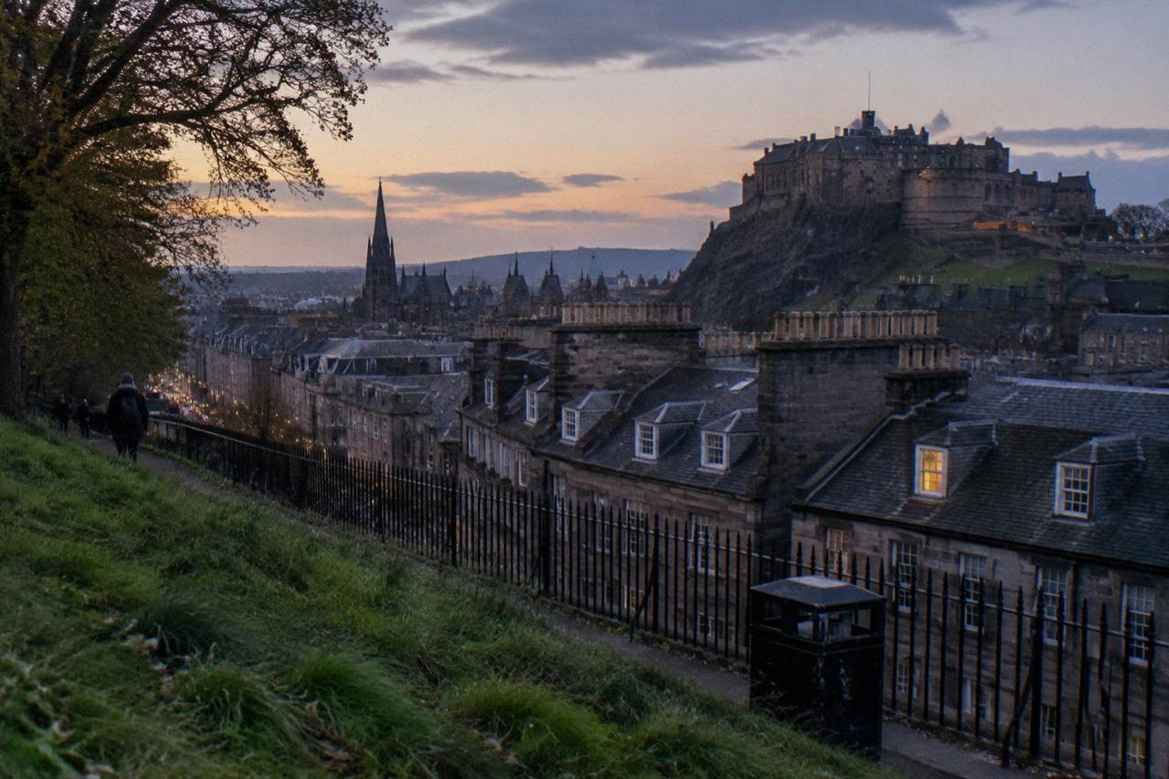 Edinburgh Old Town rooftops and castle seen from a green hillside at dusk