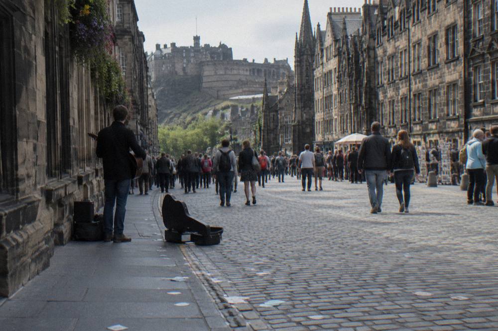 Crowded Royal Mile street lined with festival signage and stone buildings in summer