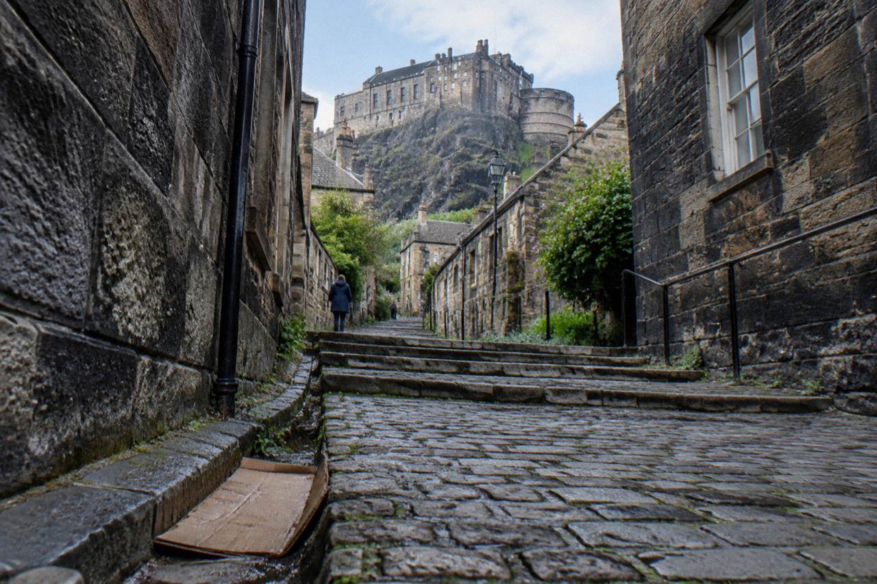 Cobbled close with tenement buildings rising toward Edinburgh Castle on a bright morning