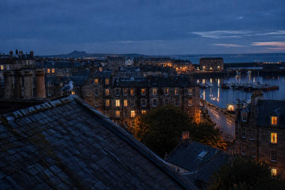 Edinburgh evening skyline with lit tenement windows above rooftops