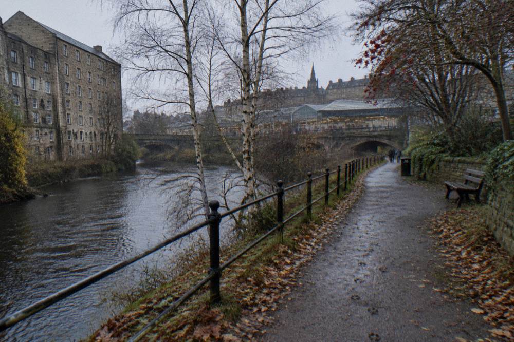 A wooded riverside path beside the Water of Leith with stone buildings in the background