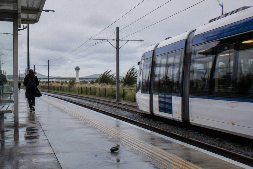 A tram at a station platform with a person walking nearby, no stone buildings visible