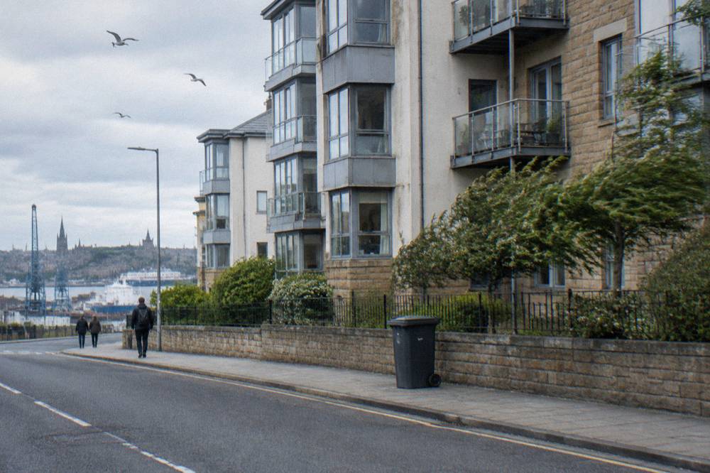 Exterior street view of modern Edinburgh apartment buildings with pedestrians and harbour cranes in the distance
