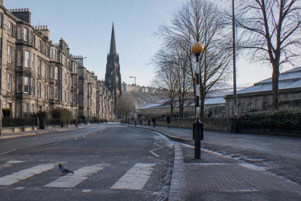 Stone terraced buildings on a wide Edinburgh street with a church spire behind