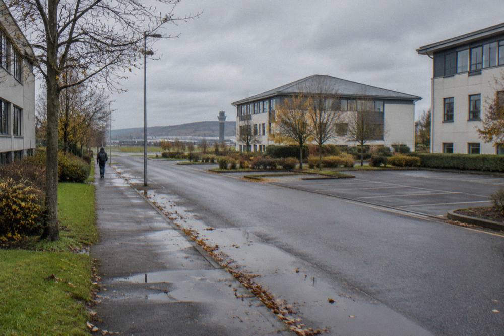 Modern office buildings beside a wet road with an airport control tower in the distance