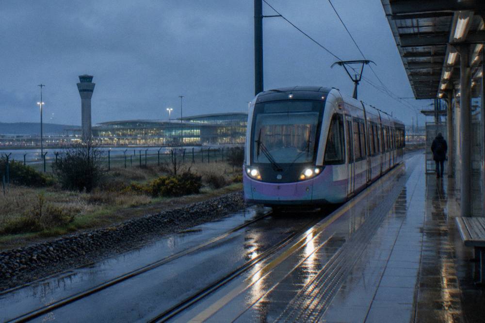 Edinburgh Airport tram stop platform with a tram arriving and terminal buildings behind