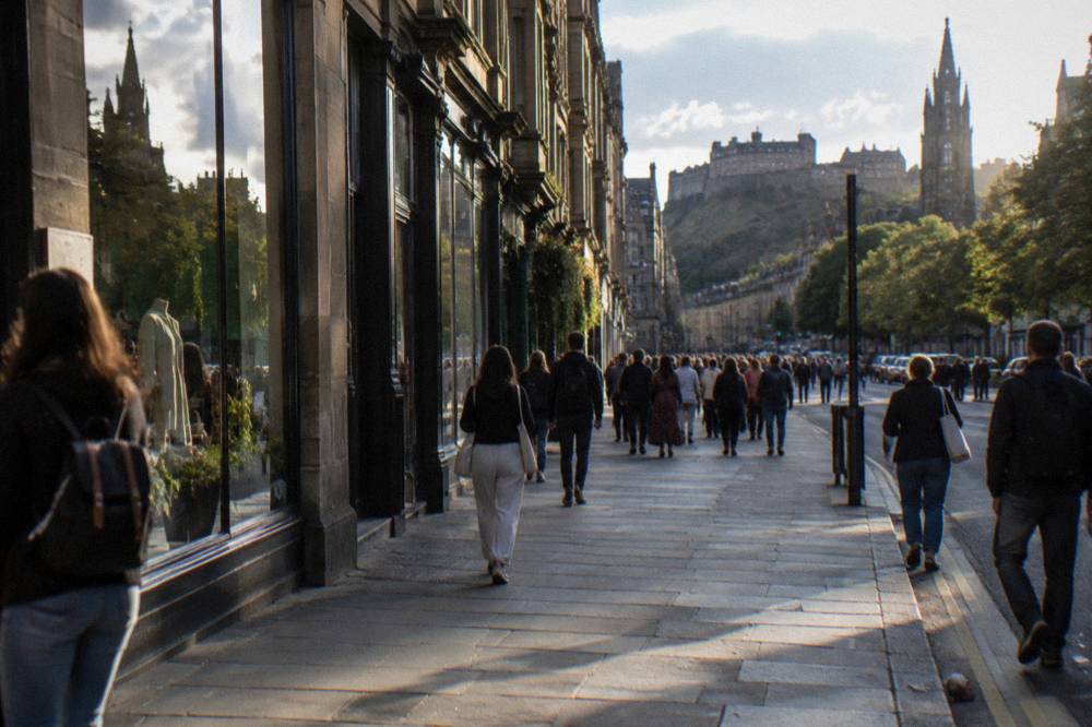 Shop fronts and terrace buildings along a busy Edinburgh street in daylight