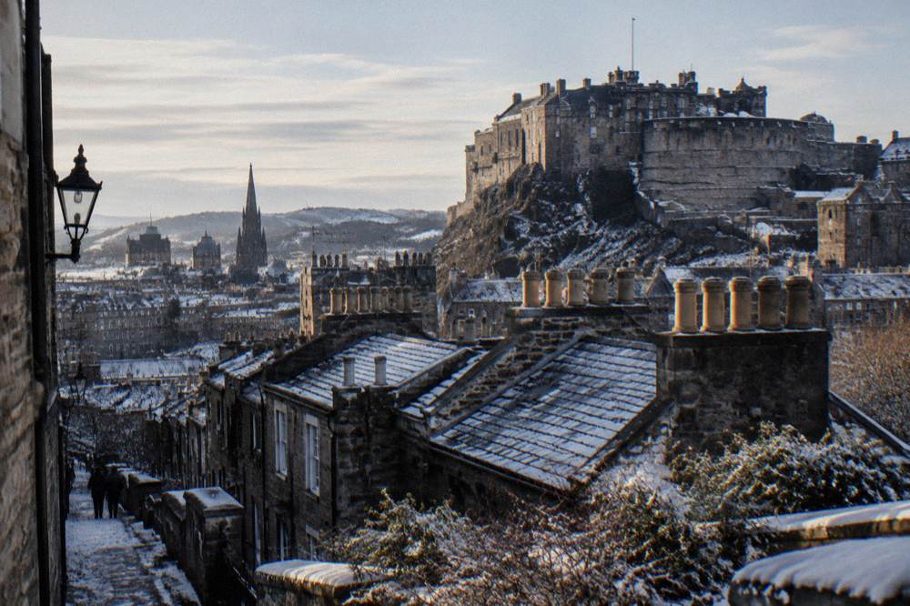 Snow-dusted rooftop view over old town rooftops toward a lit castle