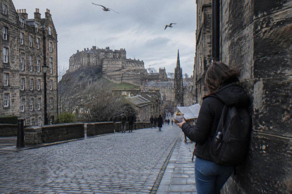 Woman with backpack reading a paper map on a cobbled street with a castle