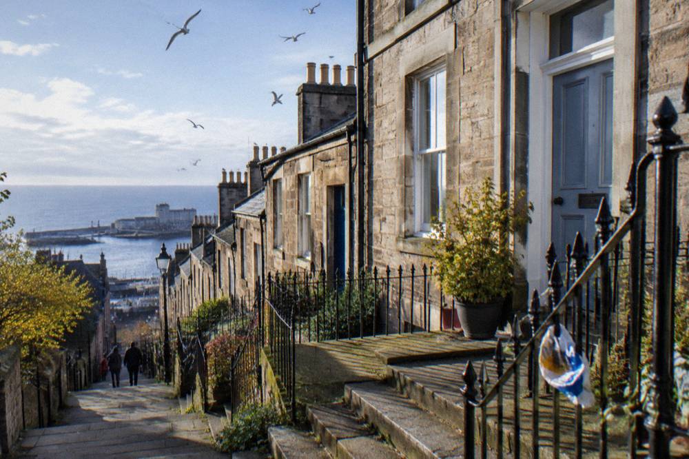 Row of sandstone terraced guest houses with steps up to front doors on a quiet Edinburgh street