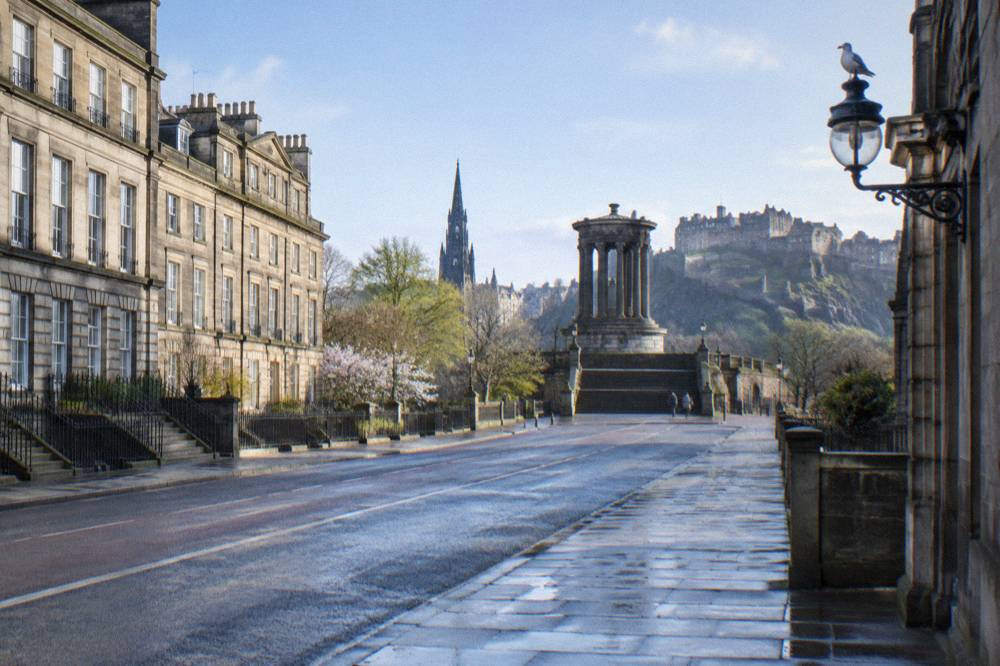 Wet street with Georgian stone facades leading to a hilltop monument and castle in the distance