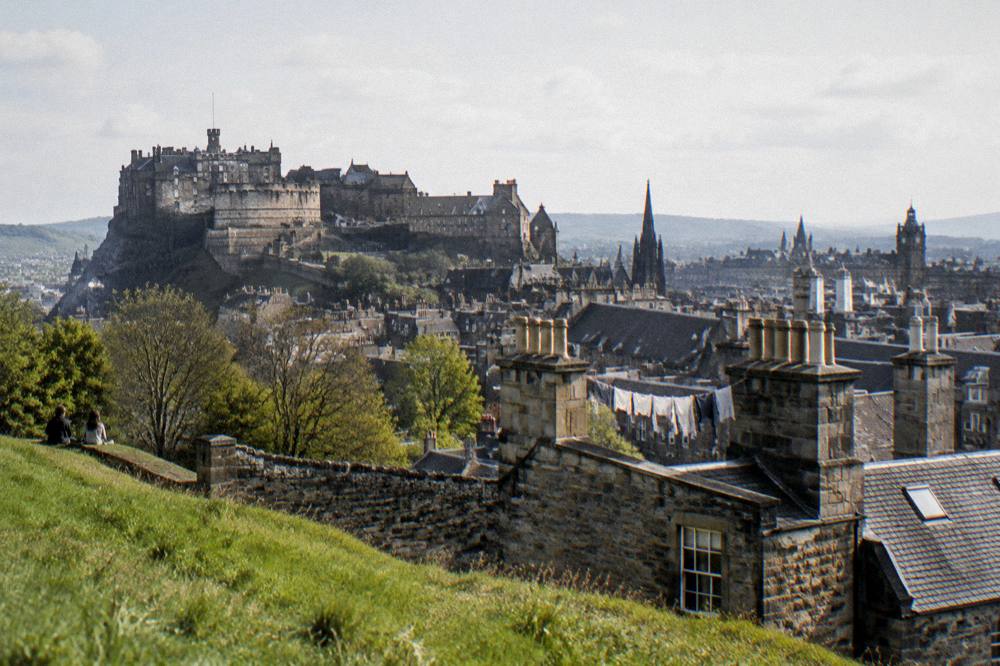 Sunlit Edinburgh skyline with castle and spires seen from a green hill